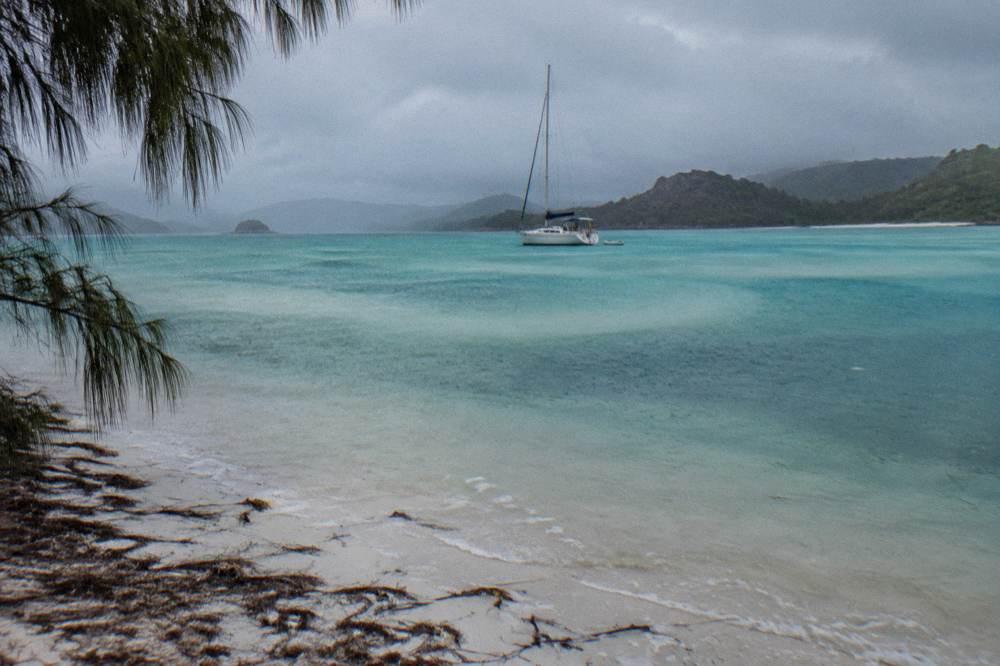 A white sailing yacht anchored off a long silica sand beach with swirling turquoise shallows
